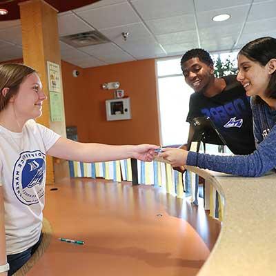 students talk to a worker at a Helpdesk inside a dorm lobby